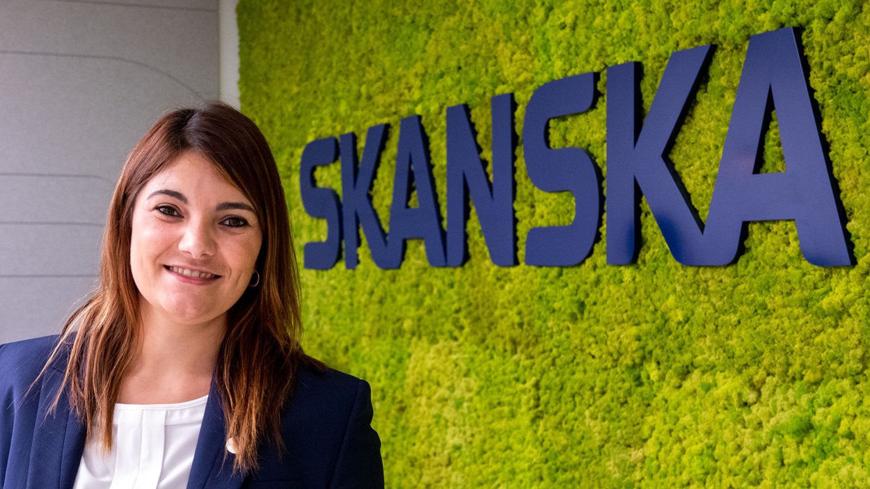 A smiling woman in an office by a large Skanska sign